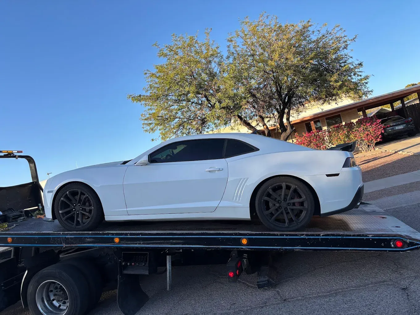 White sports car secured on a flatbed tow truck under a clear blue sky